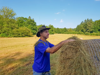 Naklejka na ściany i meble A farmer in a hat stands at a stack of fresh hay