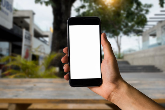 Mockup image of hand holding white mobile phone with blank white screen in garden.