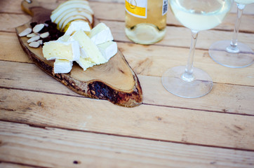 wooden slats table with bottle and glasses of white wine and snacks such as cheese, fruit and nuts