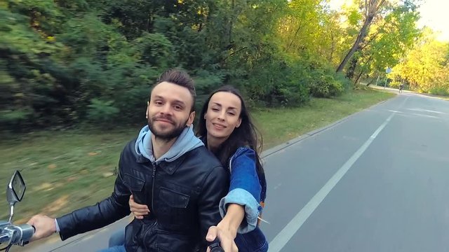 Happy couple riding on the scooter. Woman holding selfiestick and shooting video on the actioncamera.
