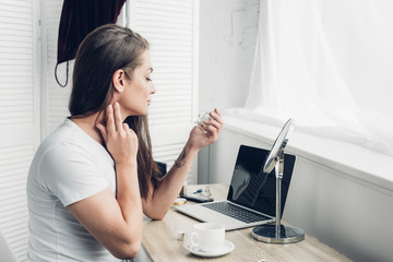 young transgender man applying perfume on neck at workplace