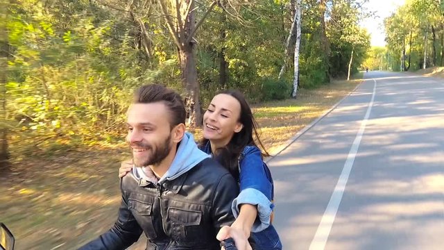 Happy couple riding on the scooter. Man driving, woman holding selfiestick and shooting video on the actioncamera.