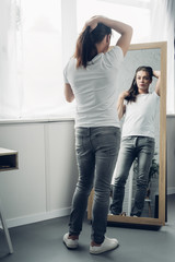 transgender woman in white t-shirt looking at mirror at home