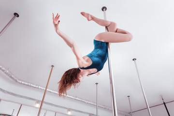Dance studio. Athletic professional pole dancer training all day in light spacious pole dance studio