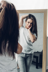 young transgender man in white t-shirt looking at mirror at home
