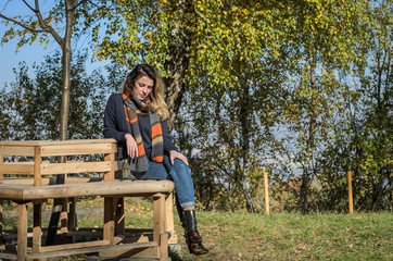 Naklejka na ściany i meble Young charming girl sitting on a bench in the autumn park