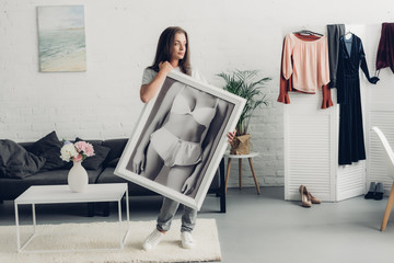 thoughtful young transgender woman holding black and white photo with female body in underwear at...