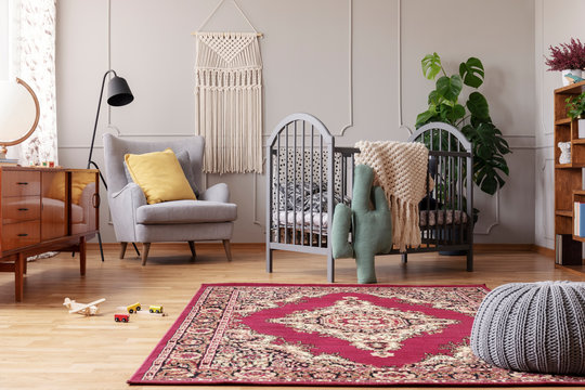 Rustic rug in stylish baby bedroom with grey and vintage furniture, real photo with copy space