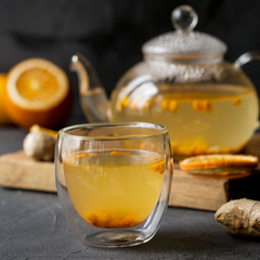 Sea buck thorn tea in glass teapot with glass cup, orange and ginger near on black background
