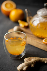 Sea buck thorn tea in glass teapot with glass cup, orange and ginger near on black background