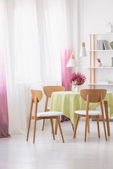 Table with lemon water, fresh heather and green tablecloth in real photo of dining room interior with lamps, window with curtains and rack with decor and books
