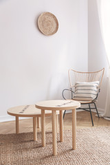 Two small coffee tables and wicker chair with pillow on it in natural beige living room - obrazy, fototapety, plakaty