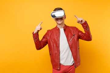 Portrait vogue handsome young man in red leather jacket, t-shirt looking in headset standing isolated on bright trending yellow background. People sincere emotions lifestyle concept. Advertising area.