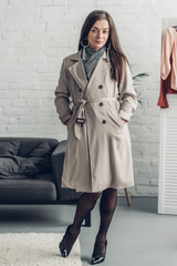 young transgender woman in trench coat looking at camera at home