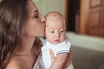 Beautiful young mother holds the baby in her arms. Mom holds the baby's legs in her hands for 3 months. Love. Motherhood. Happiness. House. Cozy.