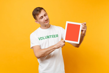 Man in white t-shirt written inscription green title volunteer hold tablet pc computer with blank empty screen isolated on yellow background. Voluntary free assistance help, charity grace work concept