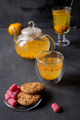 Sea buck thorn tea in glass teapot with glass cup, cookies, sweet candies near on black background