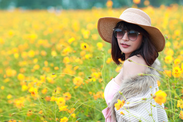 cute and beautiful girl with hat standing in nature outdoors among cosmos flowers field (rest time on vacation concept)