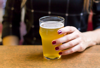 Girl holds glass of beer on the wooden table in bar, close-up