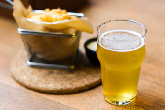 Glass of beer and snack on the wooden table in bar, close-up