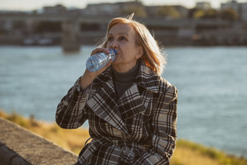 Senior woman enjoys drinking water while sitting by the river.