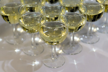 A lot of glasses with champagne stand in a triangular row on white table, closeup.