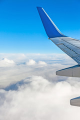 Wing of airplane from window flying over clouds in blue sky, journey concept