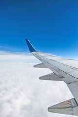 Wing of airplane from window flying over clouds in blue sky, journey concept