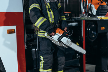 partial view of firefighter in protective uniform holding electric saw in hands at fire station