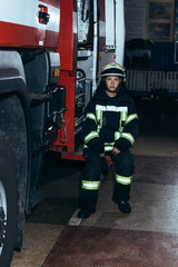 female firefighter in protective uniform with portable radio set sitting on truck at fire department