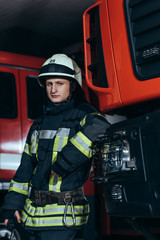 Obraz premium portret strażaka w mundurze i kasku, opierając się na ciężarówce w remizie