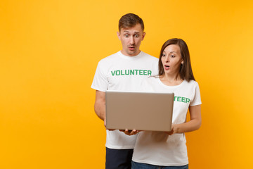 Fototapeta na wymiar Colleagues couple in white t-shirt with inscription green volunteer using typing laptop pc computer isolated on yellow background. Voluntary free work, assistance help, charity grace teamwork concept.