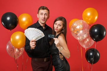 Fototapeta premium Fun couple celebrating birthday holiday party hold lot cash money, credit card isolated on bright red background air balloons St. Valentine International Women Day Happy New Year 2019 concept. Mock up