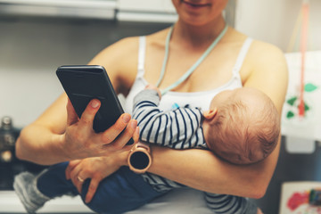 mother is using smartphone while holding infant baby © ronstik