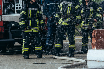 partial view of brigade of firefighters and water hose on ground on street