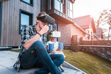 Modern family. Modern father and daughter eating popcorn and trying virtual reality glasses outside the house
