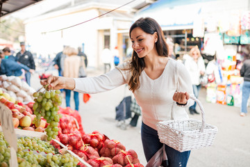 Beautiful young woman buying grapes at local food market.