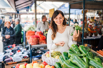 Young woman choosing vegetables on a local food market.