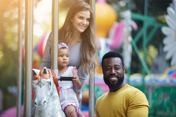 African American father and a white mother with a daughter in her arms. Family on the carousel