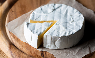 Brie type of cheese. Camembert cheese. Fresh Brie cheese and a slice on a wooden board with nuts, honey and leaves. Italian, French cheese.
