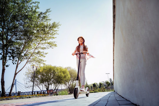 Active interaction. Cheerful girl keeping smile on her face while standing on push-cycle