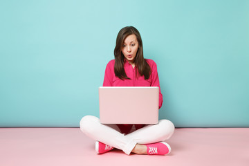 Full length portrait of young woman in rose shirt blouse white pants sitting on floor using laptop...