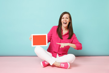 Full length portrait woman in rose shirt blouse, white pants sitting on floor hold tablet pc isolated on bright pink blue pastel wall background studio. Fashion lifestyle concept. Mock up copy space.