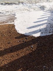 Wave of the sea on the sand beach. Shadows of wave breakers casting on the surface of the beach and water.