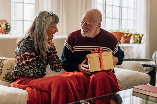 Senior couple sitting at home with a christmas present