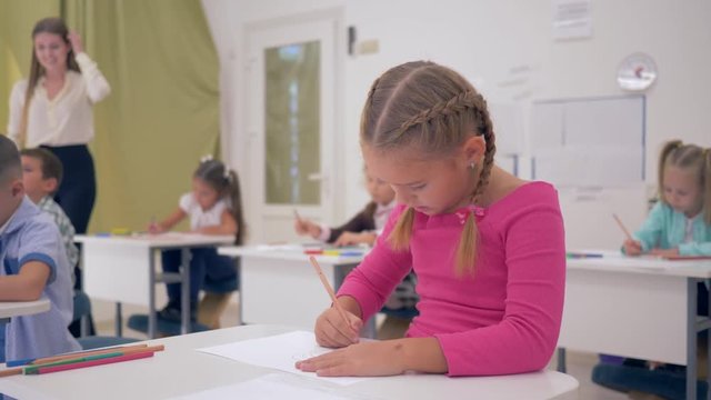 schoolgirl draws with pencils on paper and then looks at the camera with a smile at the drawing lesson in a light classroom