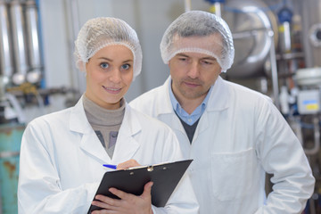 Man and woman wearing hair nets making notes on clipboard