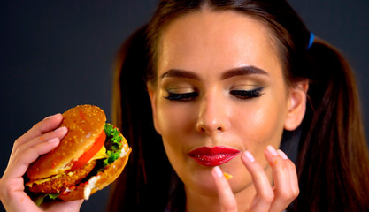 Woman bite big hamburger. Girl eat fast food and lick your fingers . How to save lipstick while eating.