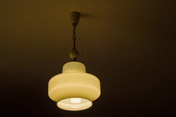 The light of the retro chandelier (white glass) suspended on chains to the ceiling at night. Close-up