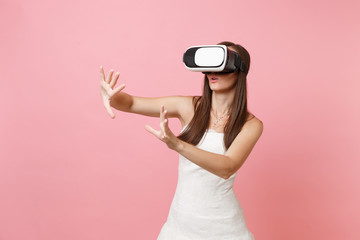 Bride woman in white wedding dress, headset of virtual reality touch something like push on button or pointing at floating virtual screen isolated on pastel pink background. Organization of wedding.